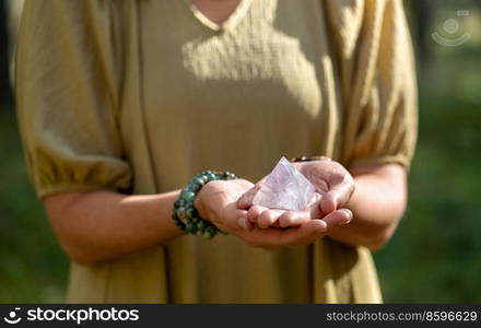 occult science and supernatural concept - close up of woman or witch with semiprecious crystal or gemstone pyramid performing magic ritual in forest. close up of woman holding crystal pyramid