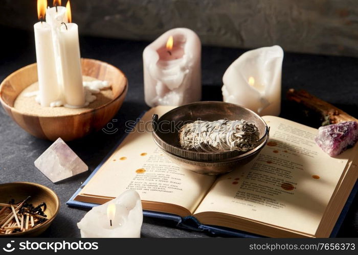 occult science and supernatural concept - magic book, white sage, burning candles and different staff for ritual. magic book, sage, burning candles and ritual staff