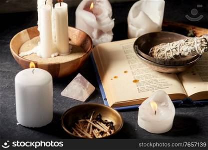 occult science and supernatural concept - magic book, white sage, burning candles and different staff for ritual. magic book, sage, burning candles and ritual staff