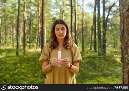 occult science and supernatural concept - young woman or witch with candle performing magic ritual in forest. woman or witch performing magic ritual in forest