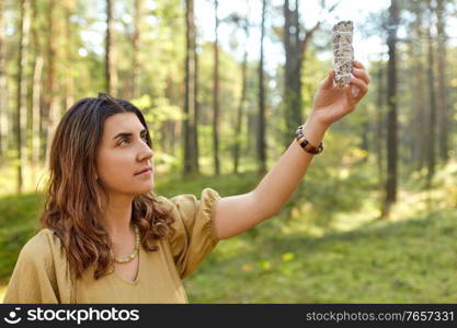 occult science and supernatural concept - young woman or witch with smoking white sage performing magic ritual in forest. woman or witch performing magic ritual in forest