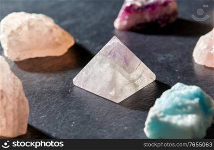 occult science, minerals and geology concept - quartz crystal pyramid and gem stones on slate background. quartz crystal pyramid and gem stones on slate