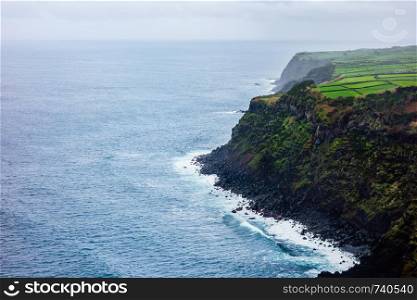 Ocean at high cliffs with lush farms on plateau, in Azores, Portugal.