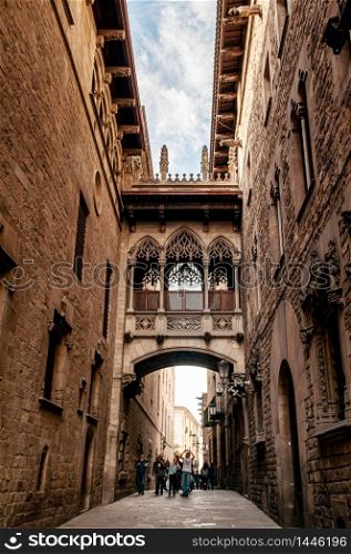 OCT 27, 2012 Bearcelona, Spain - Old ancient El Pont del Bisbe - Bishop Bridge medieval alley near Cathedral of Barcelona and tourists under warm light
