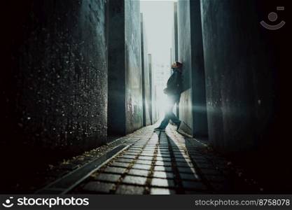 October 2021 - Berlin, Germany. Woman stands in dark maze between tall blocks in Holocaust Jewish Memorial of Murdered Jews. Light at the end of tunnel. High quality photo. October 2021 - Berlin, Germany. Woman stands in dark maze between tall blocks in Holocaust Jewish Memorial of Murdered Jews. Light at the end of tunnel.