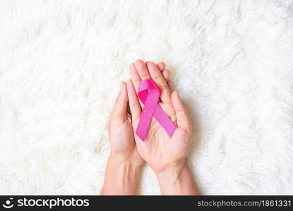 October Breast Cancer Awareness month, adult Woman hand holding Pink Ribbon on pink background for supporting people living and illness. International Women, Mother and World cancer day concept