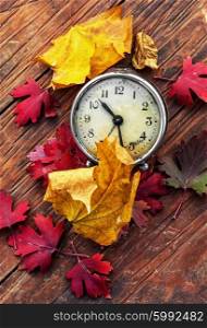 October leaves. Obsolete alarm clock on wooden background strewn with fallen leaves
