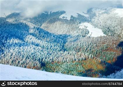 October mountain view with first winter snow and last autumn colorful foliage on far mountainside