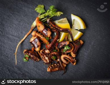 octopus salad with lemon herbs and spices on dark background top view / Tentacles squid grilled appetizer food hot and spicy chilli sauce seafood cooked served on black plate in the restaurant