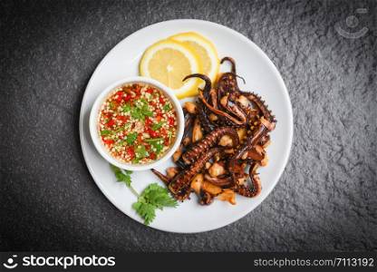 Octopus salad with lemon herbs and spices on white plate / Tentacles squid grilled appetizer food hot and spicy chilli sauce seafood cooked served on dark background , top view