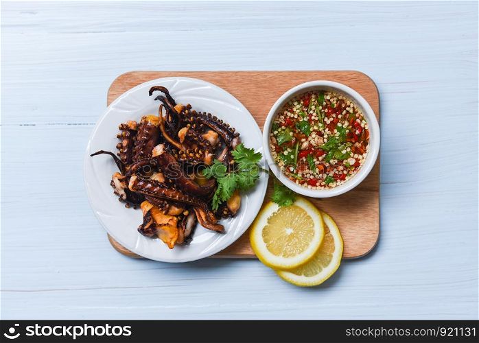 Octopus salad with lemon herbs and spices on white plate / Tentacles squid grilled appetizer food hot and spicy chilli sauce seafood cooked served on wooden background