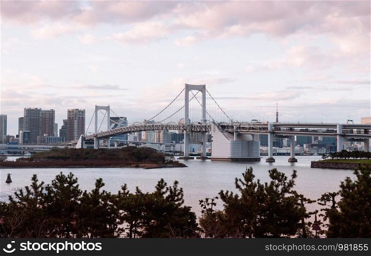Odaiba Rainbow bridge and Tokyo bay cityscape view under scattered clouds evening peaceful sky.