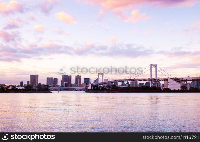 Odaiba Rainbow bridge and Tokyo bay view at evening sunset with city scape in background under pinkish sky