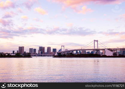 Odaiba Rainbow bridge and Tokyo bay view at evening sunset with city scape in background under pinkish sky