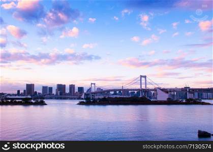 Odaiba Rainbow bridge and Tokyo bay view at evening sunset with cityscape in background under pinkish sky