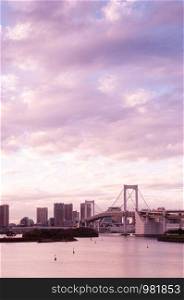 Odaiba Rainbow bridge and Tokyo bay view at evening sunset with cityscape in background under pinkish sky