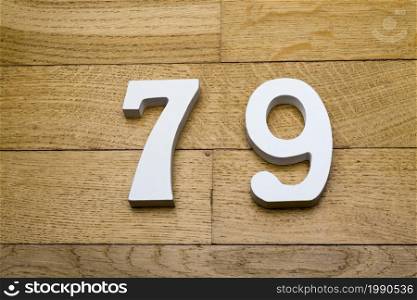 Of the numbers seventy nine on wooden parquet floor in the background.. Figures seventy-nine on a wooden, parquet floor.
