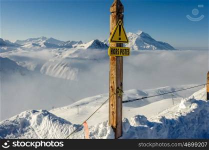 Off-piste sign in french language at Alpine winter mountain landscape with low clouds. French Alps covered with snow in sunny day. Val-d'Isere, France