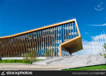 office building in the meadow with glass Windows that reflect the floating clouds, along the building there are people. The building housing the city's University Innopolis, Kazan. office building in the meadow with glass windows that reflect the floating clouds, along the building there are people