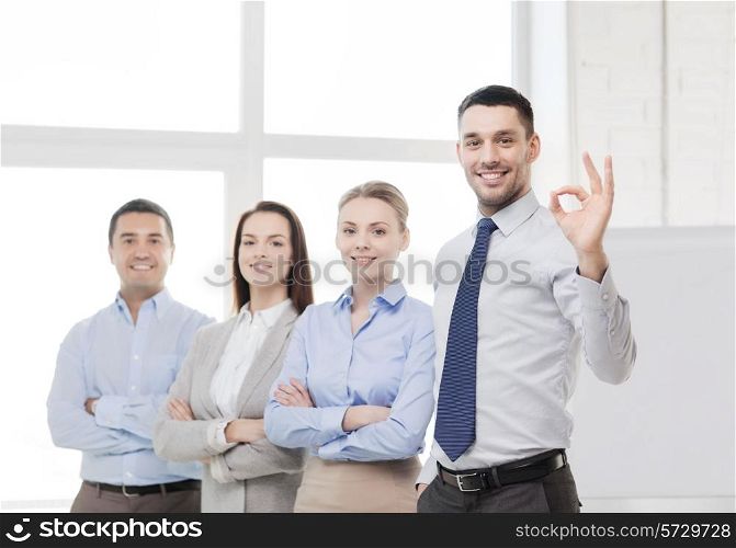 office, business, and teamwork concept - friendly young smiling businessman with team on back showing ok-sign