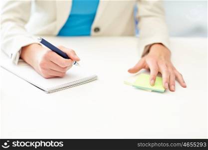 office, business, education, technology and internet concept - close up of businesswoman or student sitting at table and writing to notebook