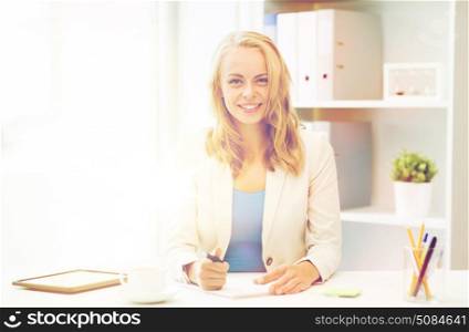 office, business, education, technology and internet concept - smiling businesswoman or student sitting at table and writing to notebook. businesswoman writing to notebook at office. businesswoman writing to notebook at office