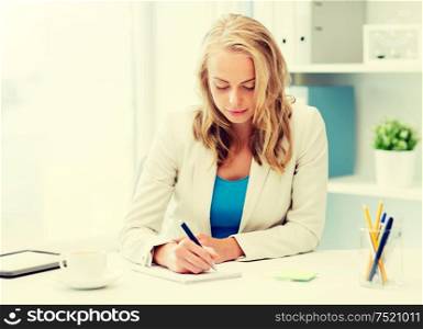 office, business, education, technology and internet concept - smiling businesswoman or student sitting at table and writing to notebook. businesswoman writing to notebook at office