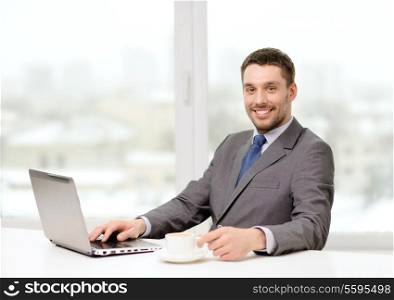 office, business, technology and internet concept - smiling businessman with laptop computer and coffee at office