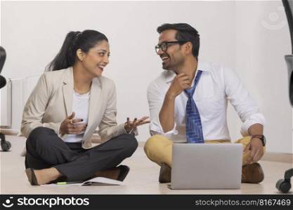 Office colleagues smiling together while sitting down on floor in office