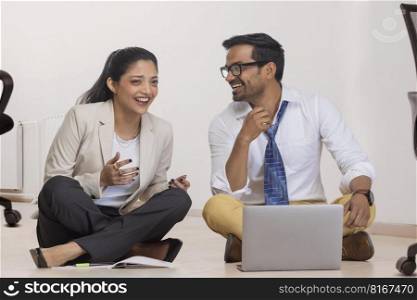 Office colleagues smiling together while sitting down on floor in office