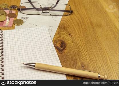 Office desk with an opened graphic notebook, a pen, some euro coins, bills and a pair of glasses