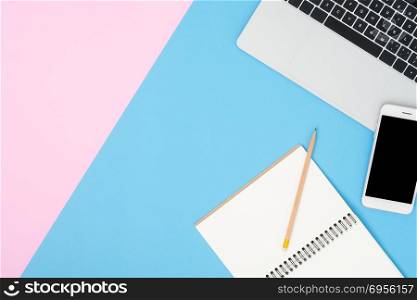 Office desk working space - Flat lay top view mockup photo of wo. Office desk working space - Flat lay top view mockup photo of working space with laptop, mock up smartphone and blank notebook on pastel background. Blue pink color background working desk concept.