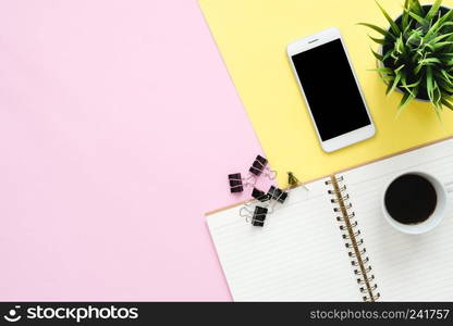 Office desk working space - Flat lay top view of a working space with white blank notebook page, coffee cup and mock up phone on pastel background. Pastel pink yellow color background space concept.