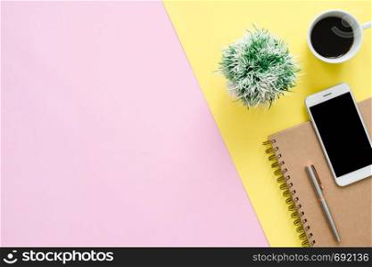 Office desk working space - Flat lay top view of a working space with white blank notebook page, coffee cup and mock up phone on pastel background. Pastel pink yellow color background space concept.