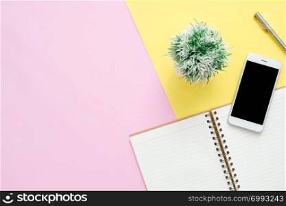 Office desk working space - Flat lay top view of a working space with white blank notebook page, plant tree and mock up phone on pastel background. Pastel pink yellow color background space concept.
