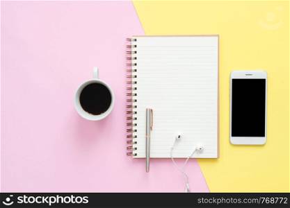 Office desk working space - Flat lay top view of working space with white blank notebook, earphone, coffee cup and mock up phone on pastel background. Pastel pink yellow color background space concept
