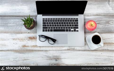 Office desktop setting with laptop plus food and drink on white rustic desk