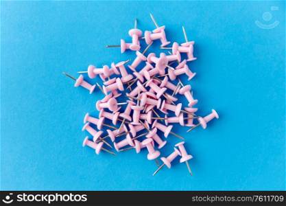 office supplies, stationery and object concept - heap of pink pins on blue background. heap of pink office pins on blue background