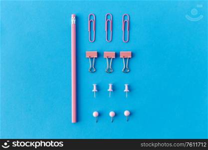 office supplies, stationery and object concept - pink pencil, pins and clips on blue background. pink pencil, pins and clips on blue background
