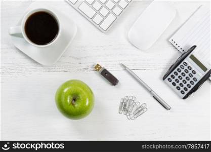 Office table with computer, notepad, thumb drive, mouse, silver pen, calculator, green apple, paper clips and black coffee. Top view angle with copy space.