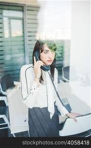Office window view of young businesswoman talking on landline