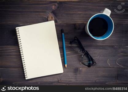 Office wood table with blank notepad, pencil, glasses and cup of coffee.