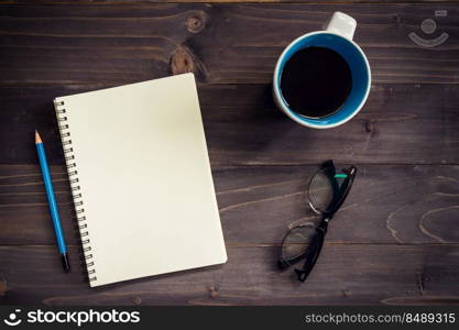 Office wood table with blank notepad, pencil, glasses and cup of coffee.