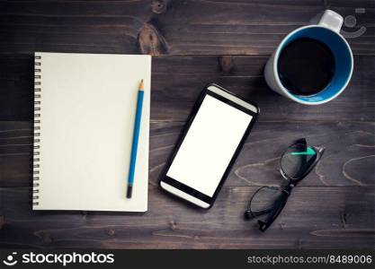 Office wood table with blank notepad, pencil, glasses, phone and white cup of coffee.