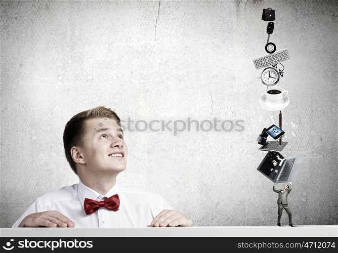 Office work. Young man looking at miniature of businessman