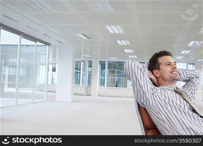 Office worker leaning back in swivel chair hands behind head in empty office space