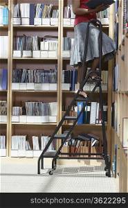 Office worker standing on ladder in file storage room, low section