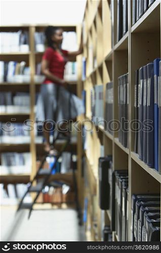 Office worker standing on ladder in file storage room, selective focus, side view
