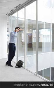 Office worker talking on mobile phone looking out window of empty office space