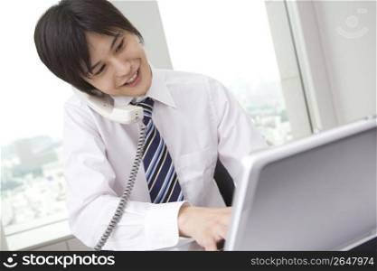 Office worker talking with phone while operating PC